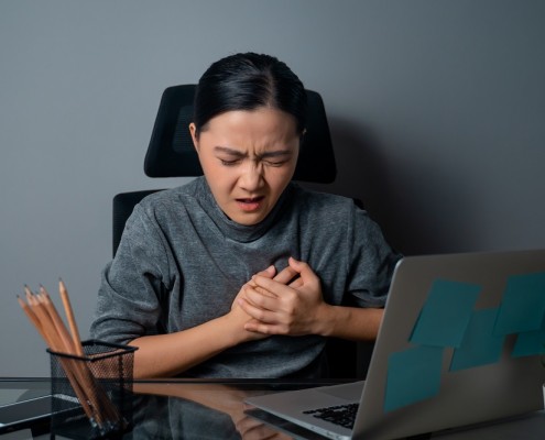 Asian woman working on a laptop was sick with chest pain sitting at office. isolated on gray background.